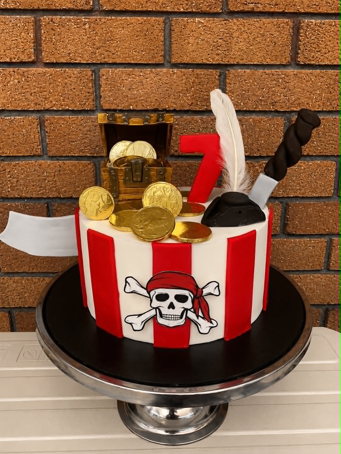 Pirate 7th birthday cake with red and white stripes, skull and crossbones, treasure chest and gold coins